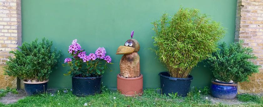 Row of potted plants with a wooden bird sculpture in the middle